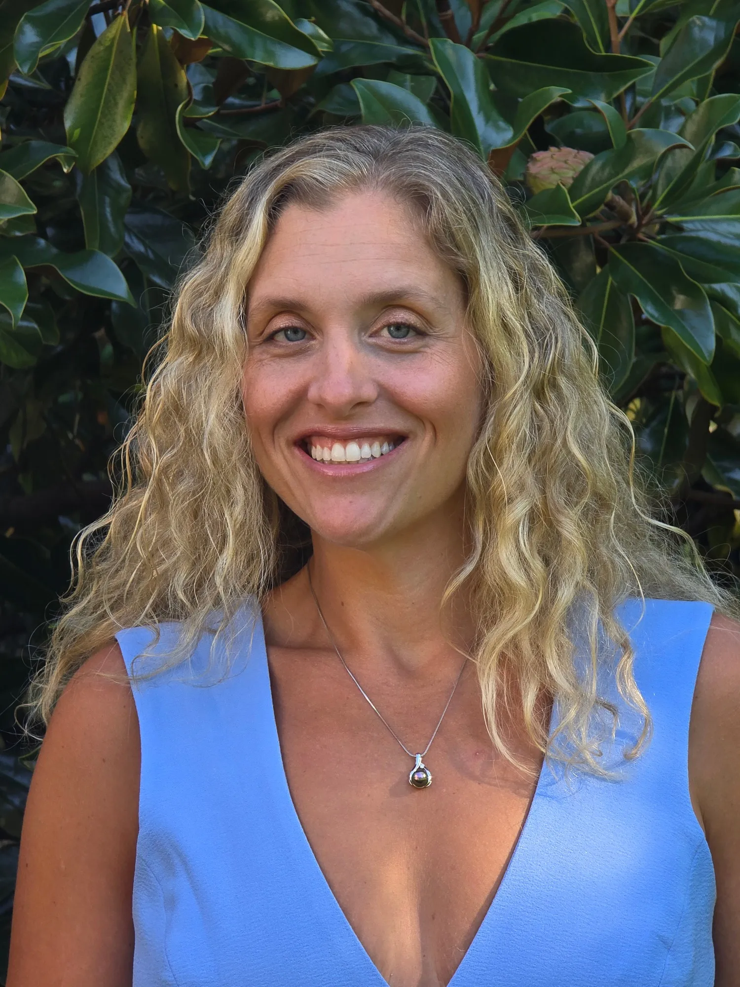 A close portrait of Nicole Lawton, smiling, with sunlit magnolia leaves behind her.